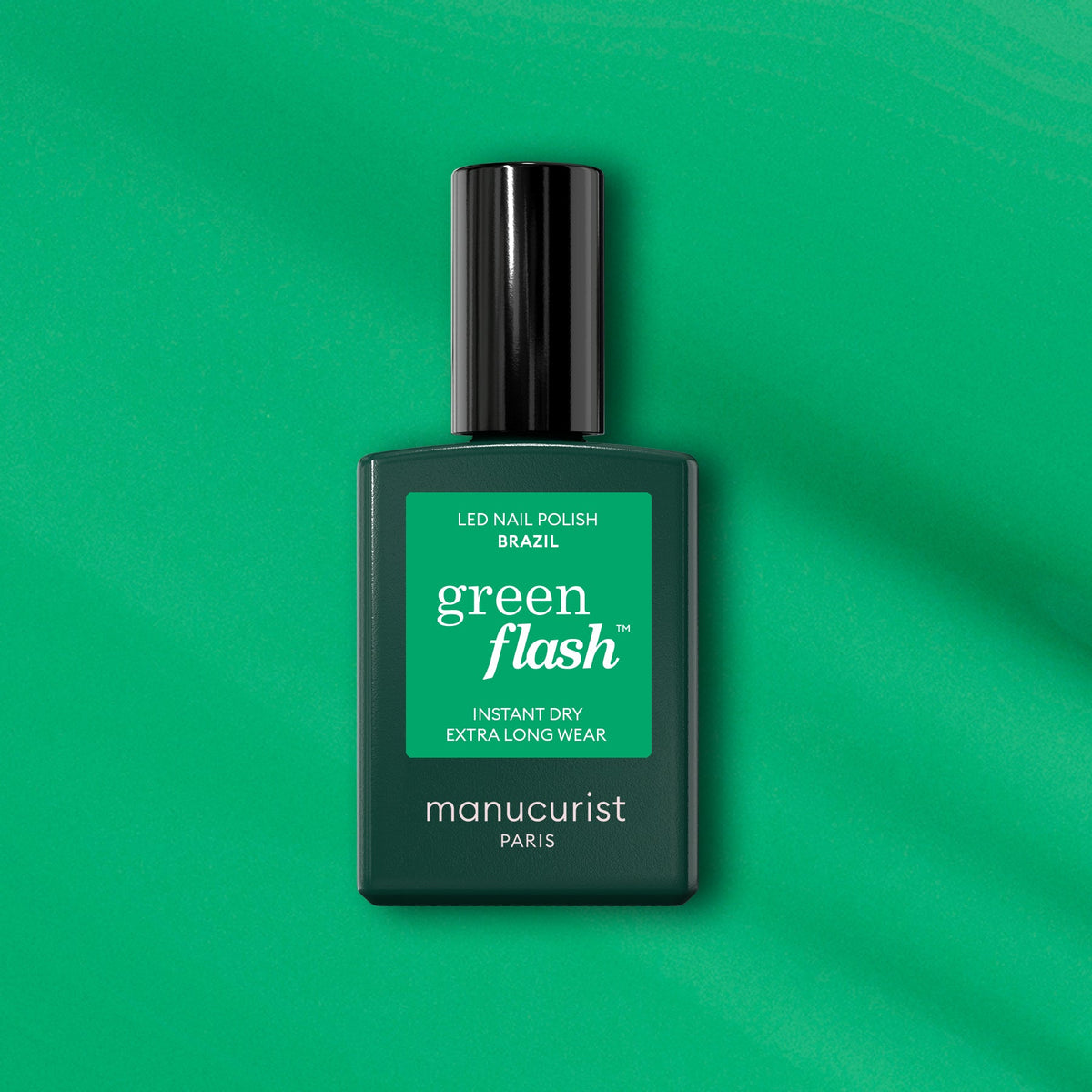 A bottle of Manucurist Brazil nail polish rests on a green surface, its bold electric green shade perfectly matching the vibrant label for a striking, cohesive appearance.