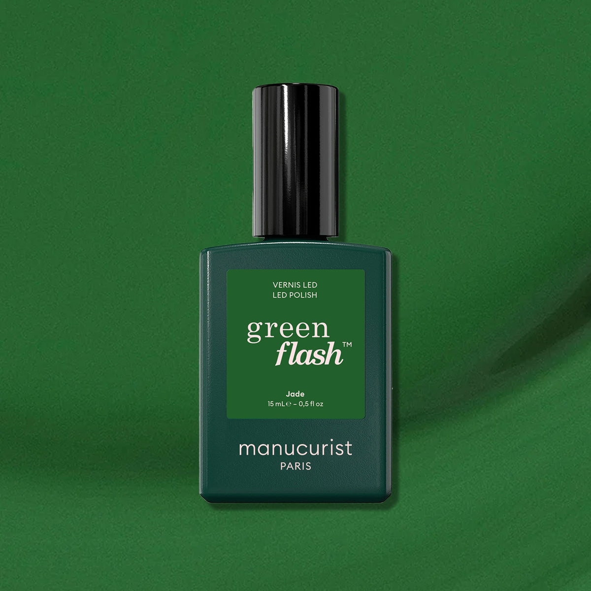 A bottle of Manucurist Jade LED gel polish stands upright on a glossy green surface with a matching mineral green background, highlighting its instant dry and extra long wear features.