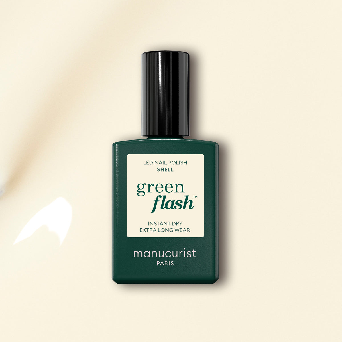 A minimalist bottle of Manucurist’s Shell Green Flash LED gel polish, with a dark green label and black cap, rests on an off-white background with subtle light reflecting.