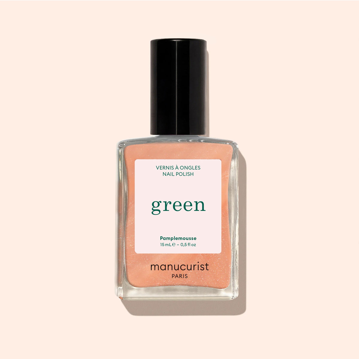 A bottle of Manucurist nail polish in the shade Pamplemousse, a pearlescent orange, with a black cap and "green" label sits against a light beige background.