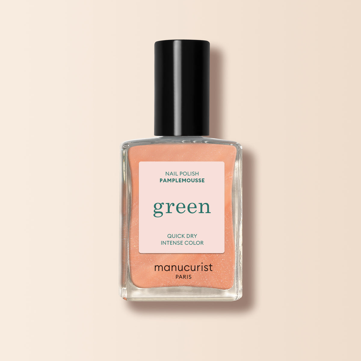 A bottle of Manucurist nail polish in the shade Pamplemousse, a pearlescent orange, with a black cap and "green" label sits against a light beige background.