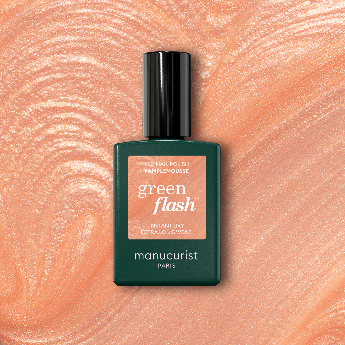 A bottle of Manucurist Pamplemousse nail polish rests on a shimmery peach-pink swirl background that reflects the shade’s tones.
