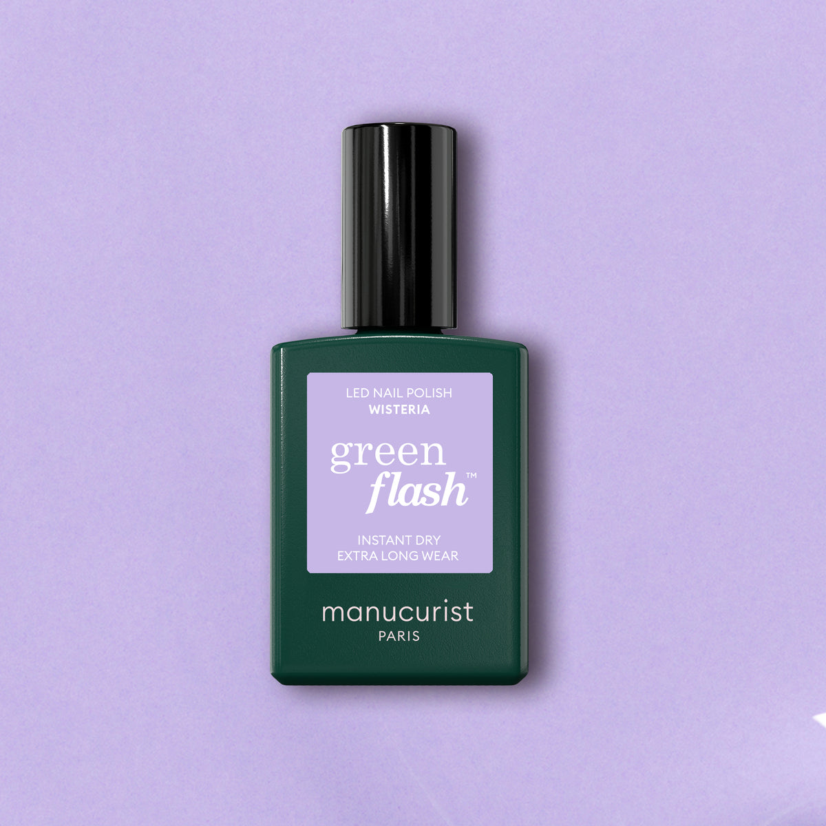 A bottle of Manucurist Wisteria gel polish stands upright against a light lavender background, its dark green bottle and black cap showcasing the pastel purple shade with a matching lavender label.