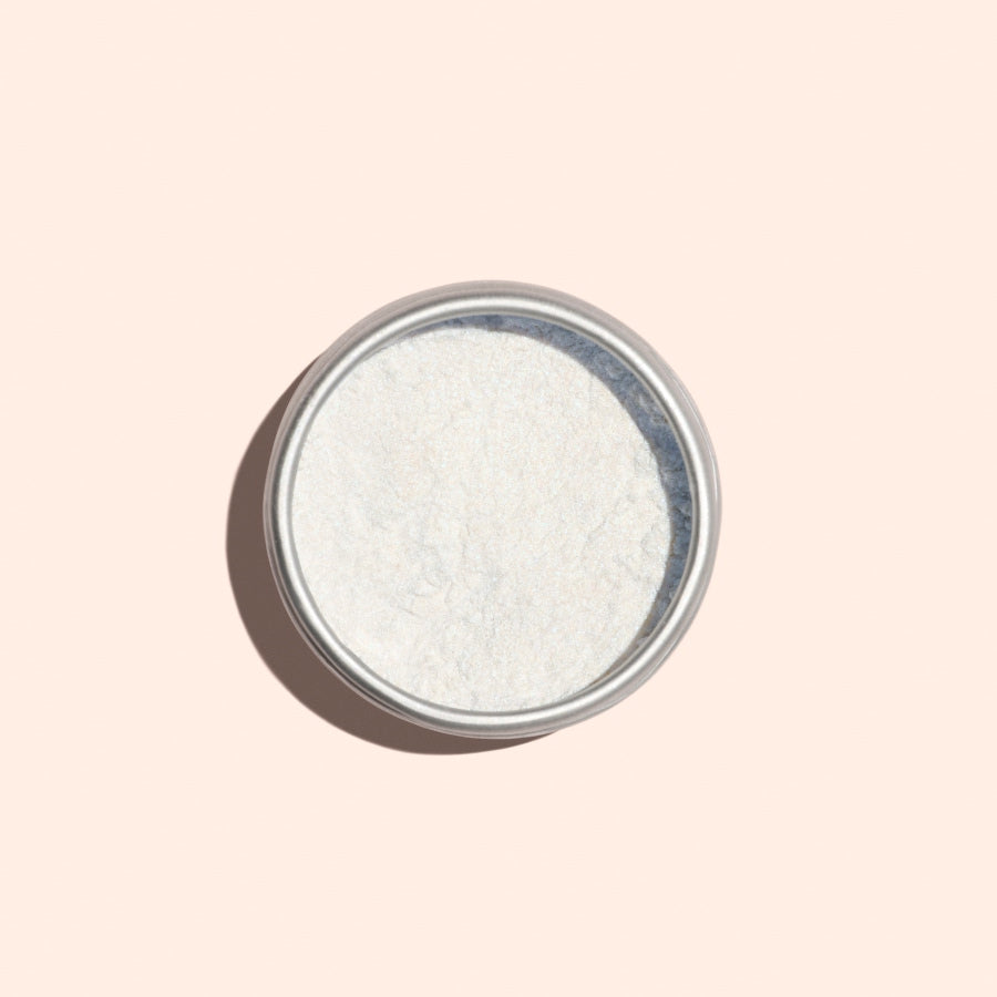 A round metal tin of Manucurist Blue Glazed Powder, a fine white manicure powder with a subtle pearly blue shimmer, is photographed from above on a light beige background.