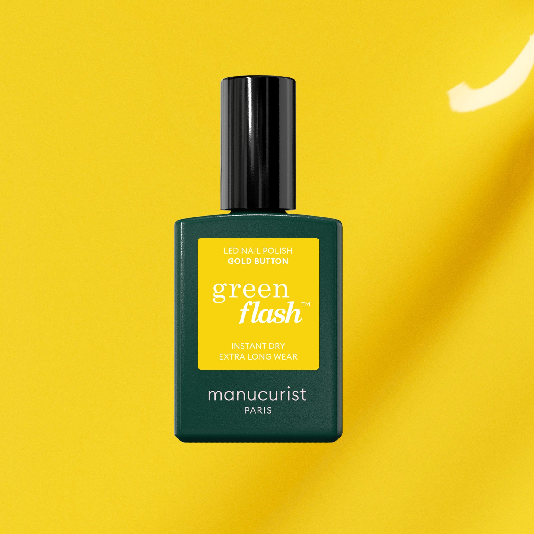 A bottle of Manucurist Gold Button gel polish with a black cap stands against a bright yellow background, highlighting its LED formula for instant dry and extra long wear, delivering standout yellow nails.