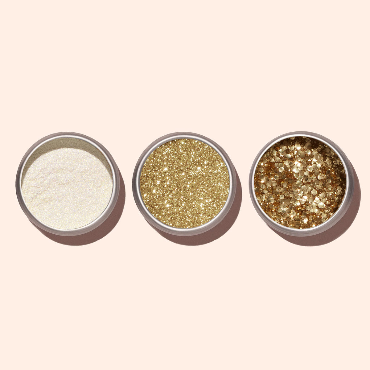Three small round containers of Manucurist Gold Biodegradable Glitter—ranging from fine to chunky textures—are arranged in a row on a light beige background, ideal for sparkling nail art.