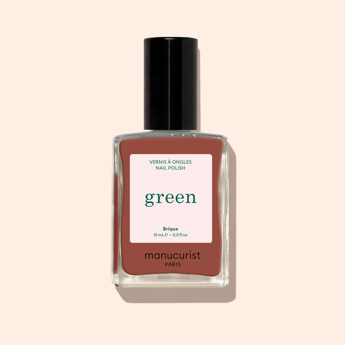 Manucurist’s Brique nail polish, a mauve-brown shade from the Green range, is shown in a black-capped bottle with a beige label featuring green and pink text, set against a light beige background.