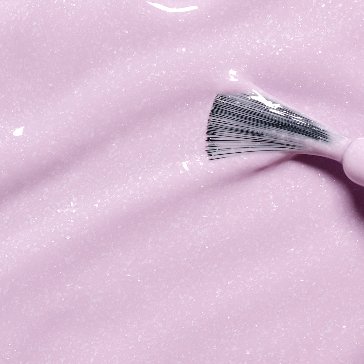 A close-up of a brush spreading Janis the Seahorse, a thick, glossy, light pink kids&