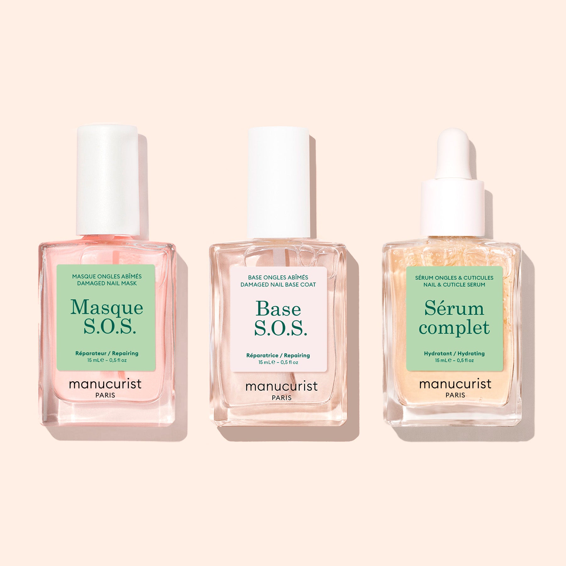 Three bottles of Manucurist nail care—S.O.S. Nail Mask, Green Base S.O.S., and Huile Verte—sit side by side on a beige background, perfect for supporting nail regeneration and repairing damaged nails.