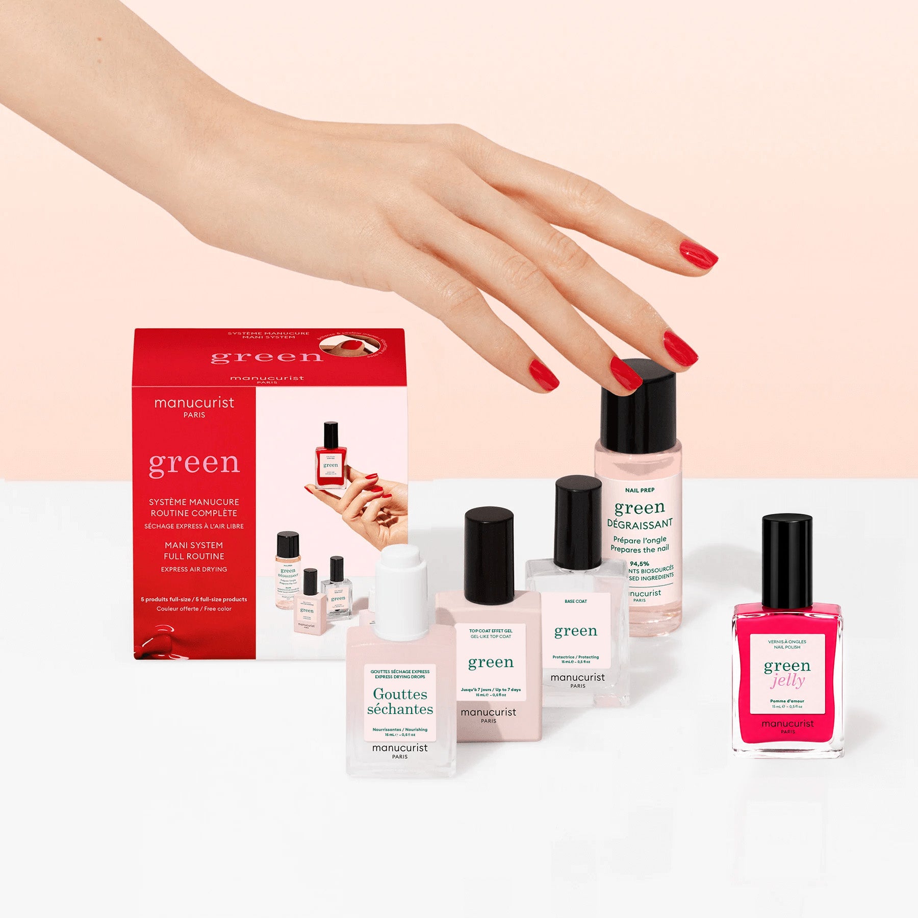 A hand with red nails reaches for manicure products, including the Manucurist Discovery Kit - Jelly Nail Polish, on a pale pink and white background.