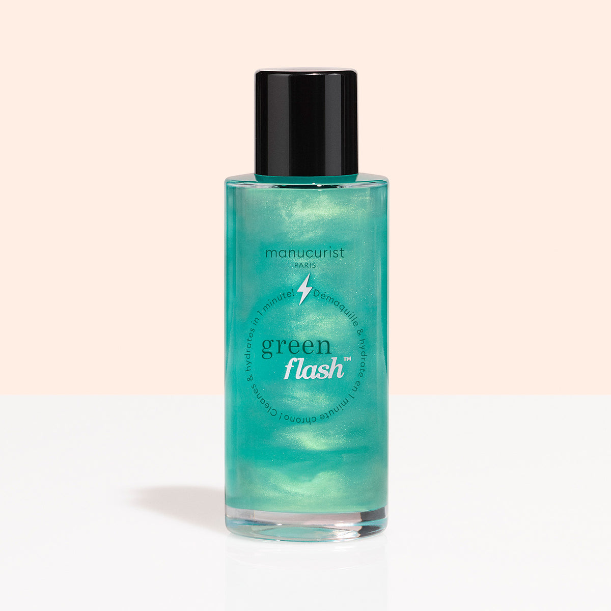 A clear bottle with a black cap holds Manucurist Green Flash™ Gentle Glitter Remover, an acetone-free formula with green liquid, shown against a light peach and white background.