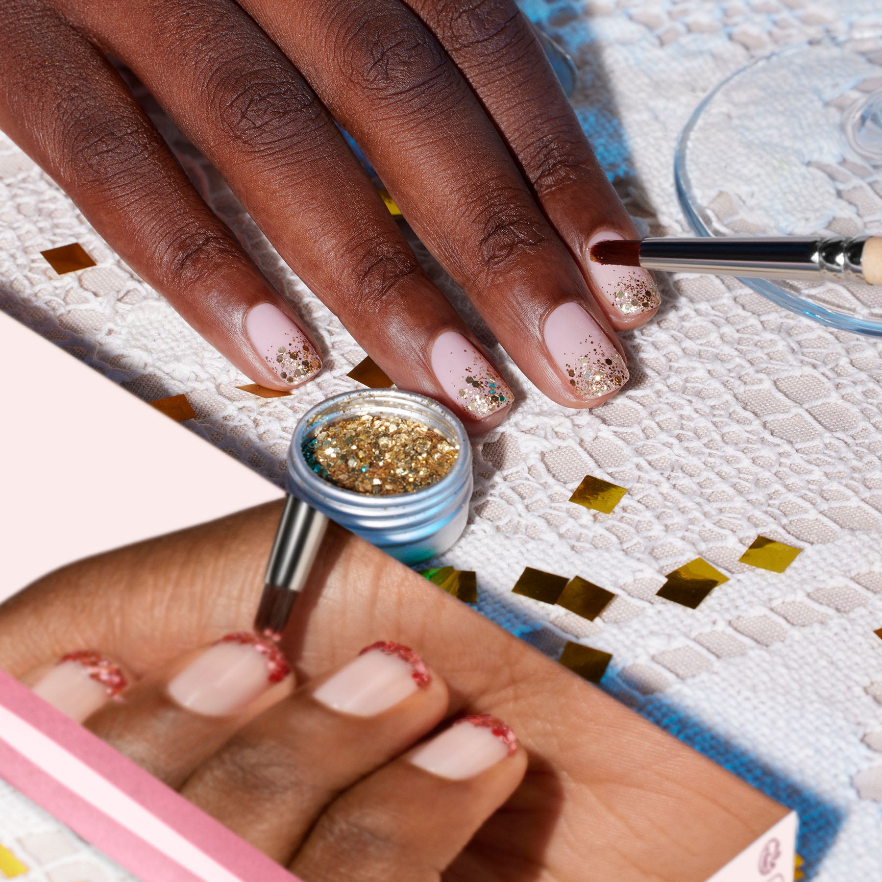 A hand with nude pink nails and gold glitter tips is painted using the Manucurist Glitter Brush with vegan bristles. Gold glitter, a manicure kit, and confetti decorate the white lace surface for a radiant finish.