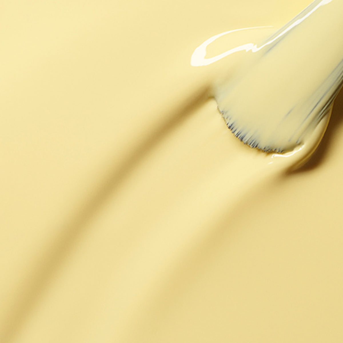 A makeup brush smoothly swirls through creamy pale yellow Flower love foundation by Manucurist, creating soft lines and texture on the surface.