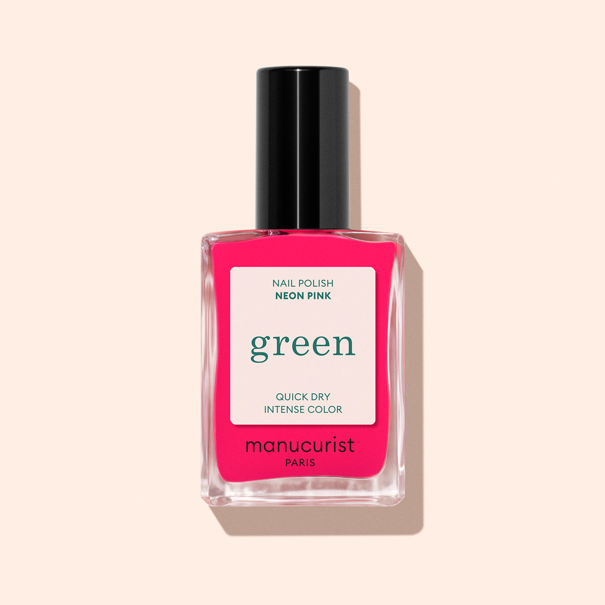 A bottle of Manucurist Neon Pink nail polish with a black cap sits on a light peach background. The label highlights its quick-dry formula and intense, vibrant color—an ideal summer nail polish choice.