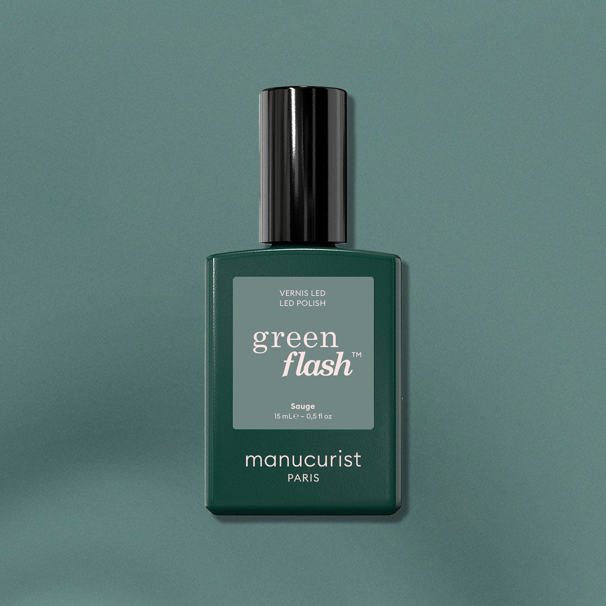 A bottle of Manucurist Sage LED nail polish, a deep sage green shade with a black cap, is displayed on a matching green surface with subtle light reflections.