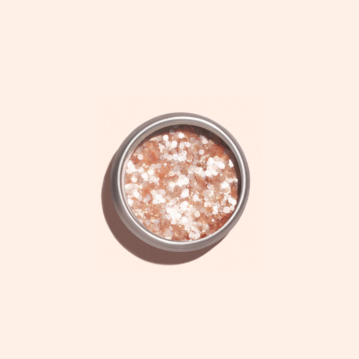A round container of Manucurist Blush biodegradable glitter features coarse pink and white crystals with eco-friendly sparkle accents, resembling bath salts or body scrub, set against a light beige background.
