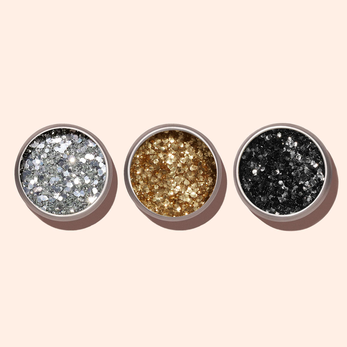 Three small round containers of Manucurist Silver biodegradable glitter for nail art are arranged in a row on a light beige background.