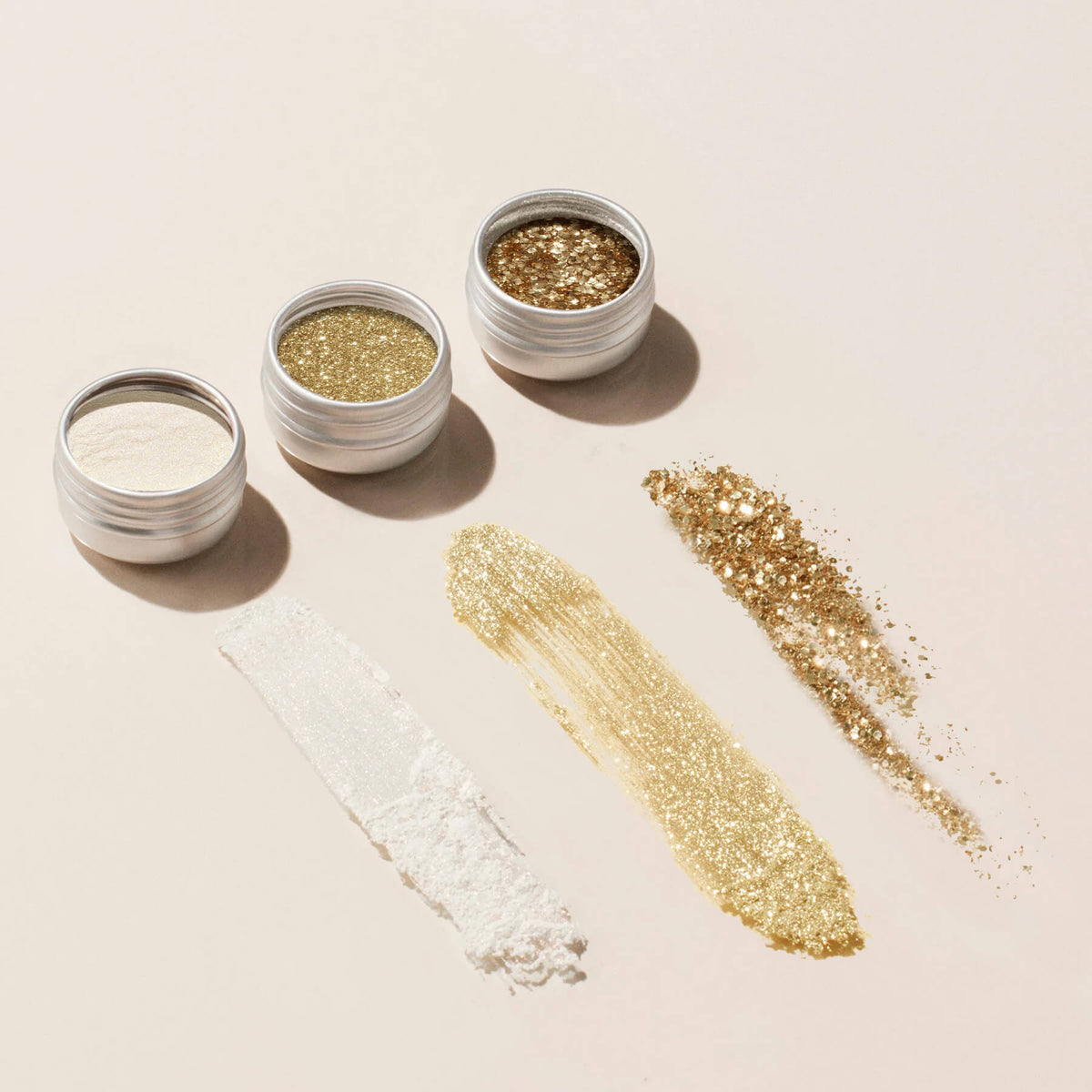 Manucurist Glitters and Effect Powders Trios—white, fine gold, and chunky gold—are shown above swatches in smooth and textured lines on a light beige surface, ideal for elevating your gel polish designs.