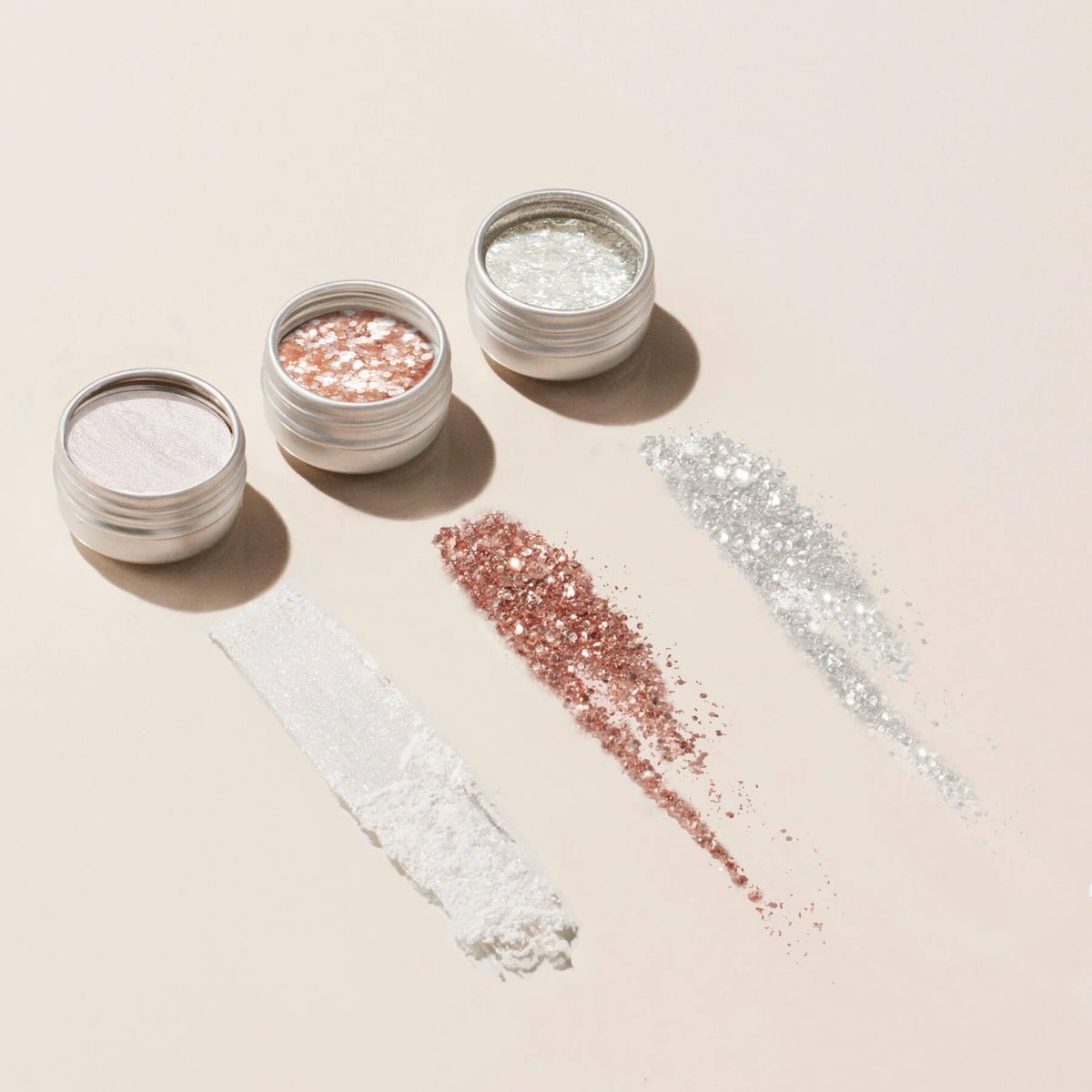 Three open Manucurist Glitters and Effect Powders Trios—white, rose gold, and silver—are displayed on a light beige background, each with matching swatches spread below the jars.