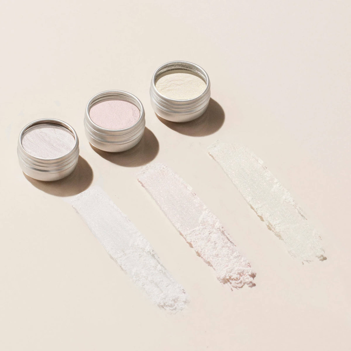 Manucurist Glitters and Effect Powders Trios: three small round containers in pastel shades—white, pale pink, and off-white—each shown with matching swatches on a beige background. Ideal for adding a subtle shimmer to your look.