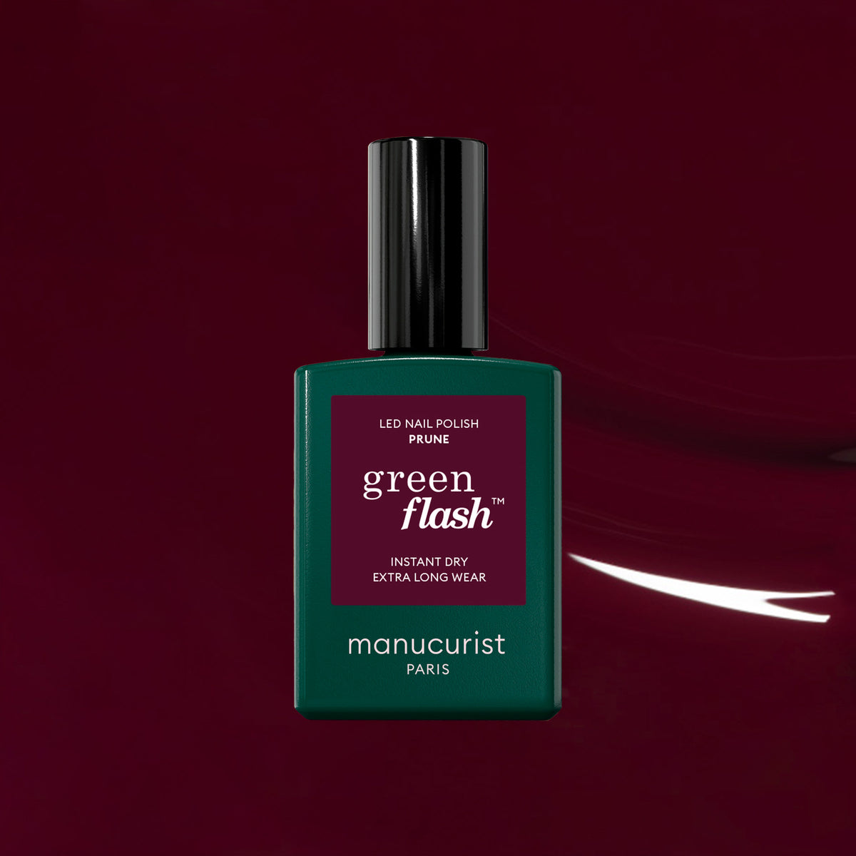 A Manucurist Prune Green Flash LED nail polish bottle, featuring a dark green body and black cap, stands against a deep wine red gel polish backdrop for a premier cru nectar-inspired allure.