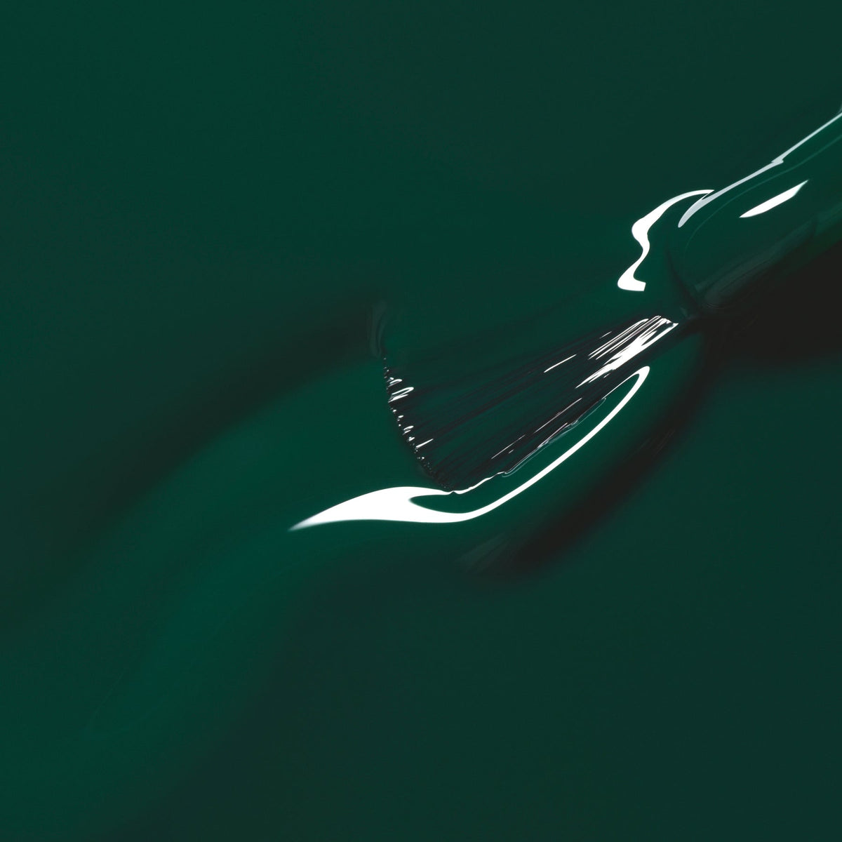 A close-up of a paintbrush applying Manucurist’s Emerald, a rich gemstone-inspired green shade, creating a smooth, glossy streak on the surface.