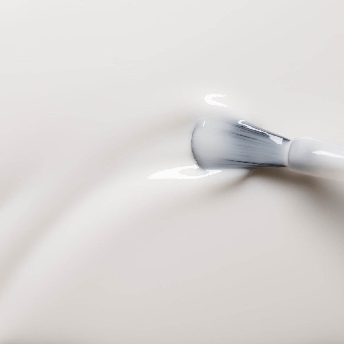 A close-up of a makeup brush with white bristles spreading Manucurist’s Milky White nail polish, creating gentle swirls and soft reflections on a smooth surface.