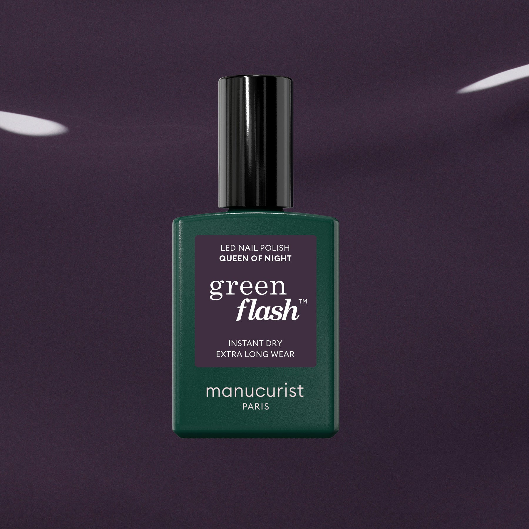A bottle of Manucurist Queen of Night gel nail polish stands against a dark, glossy backdrop. The bottle features a deep green shade, black cap, and crisp white text on the label.