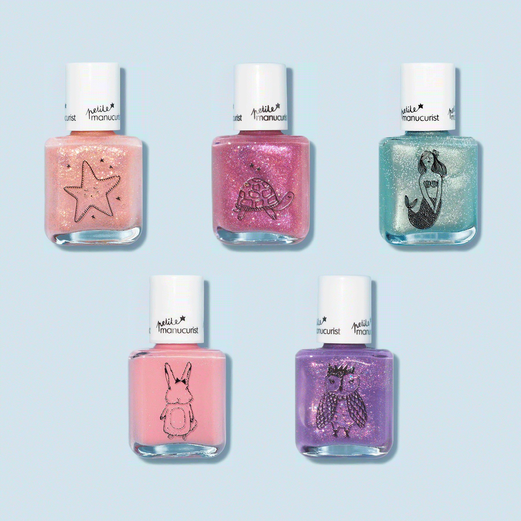 Five bottles of Customisable Rainbow Petite Manucurist kids nail polish by Manucurist, each with a white cap and cute black outline (starfish, turtle, mermaid, bunny, and owl), are arranged on a light blue background.