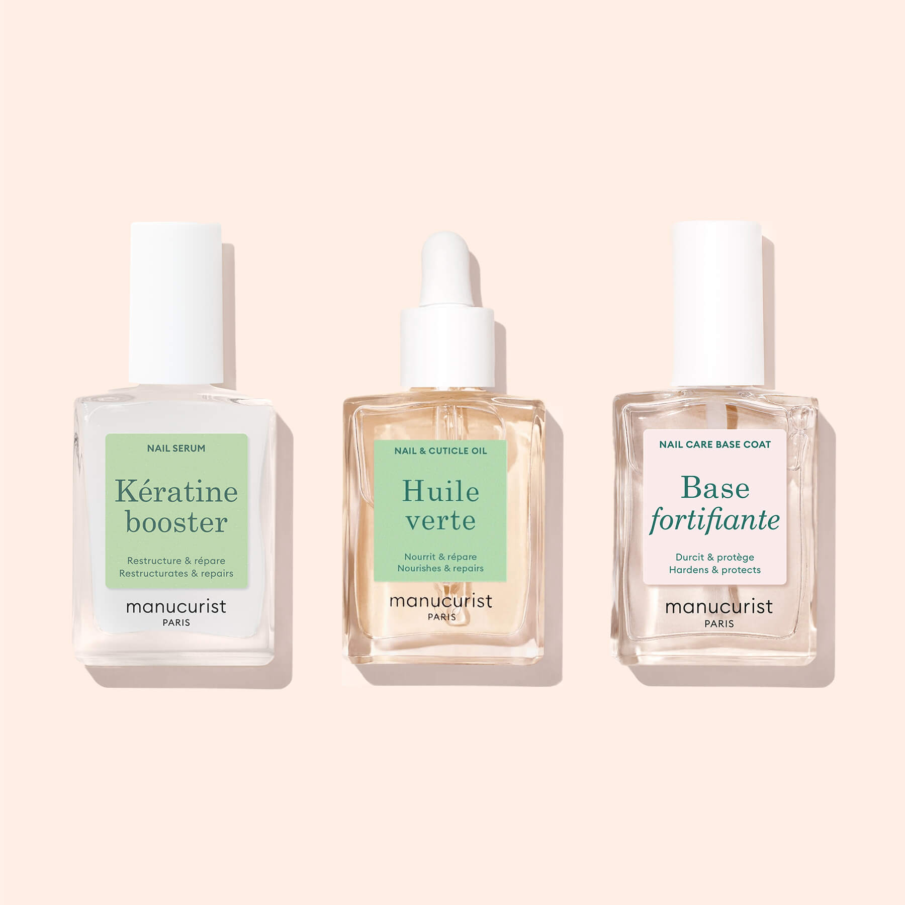 Three clear glass bottles of Manucurist’s Basic Routine - Soft Nails set with white caps are shown on a light beige background. The labels read: Keratin Booster, Nourishing Cuticle Oil (with dropper), and Base Fortifiante.