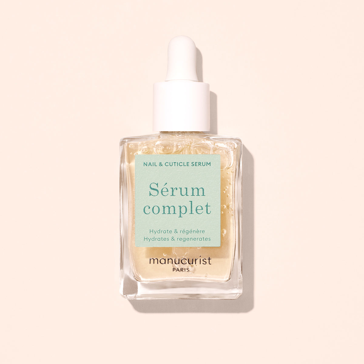 A glass dropper bottle labeled Complete Serum by Manucurist, filled with pale yellow serum for nail and cuticle care, set against a light beige background—ideal for nourishing and repairing nails.