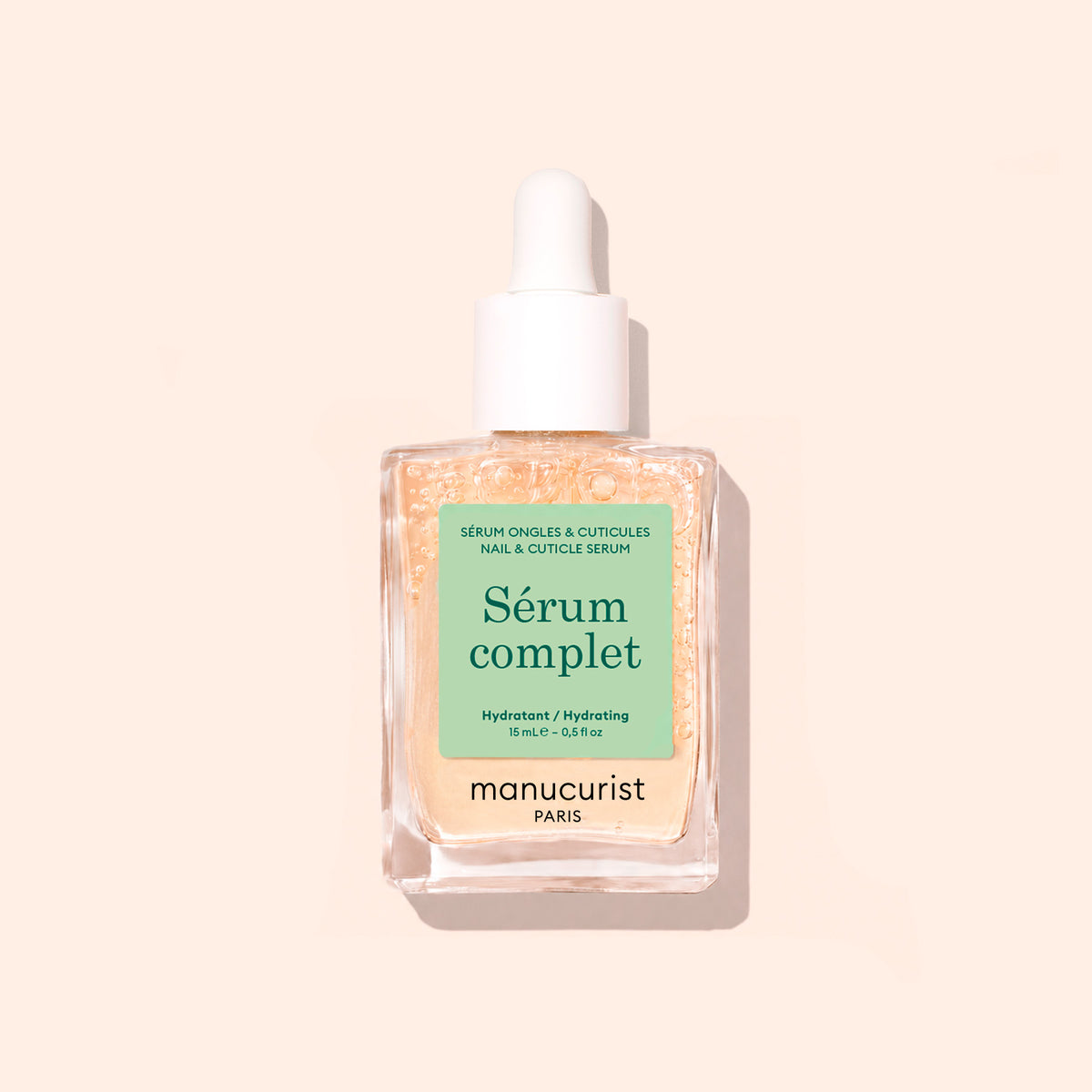 A glass dropper bottle labeled Complete Serum by Manucurist, filled with pale yellow serum for nail and cuticle care, set against a light beige background—ideal for nourishing and repairing nails.