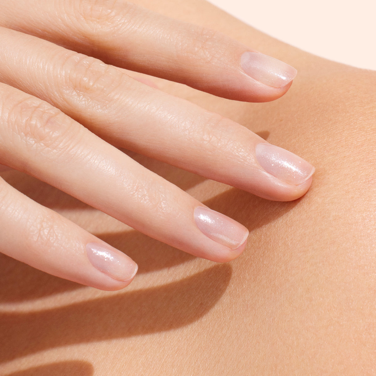 A close-up of a hand with neatly manicured, natural-looking nails featuring a subtle, sheer pink polish created with Manucurist Active™ Shine Opal, a plant-based nail polish enhanced by a nourishing nail strengthener, resting gently on smooth skin.
