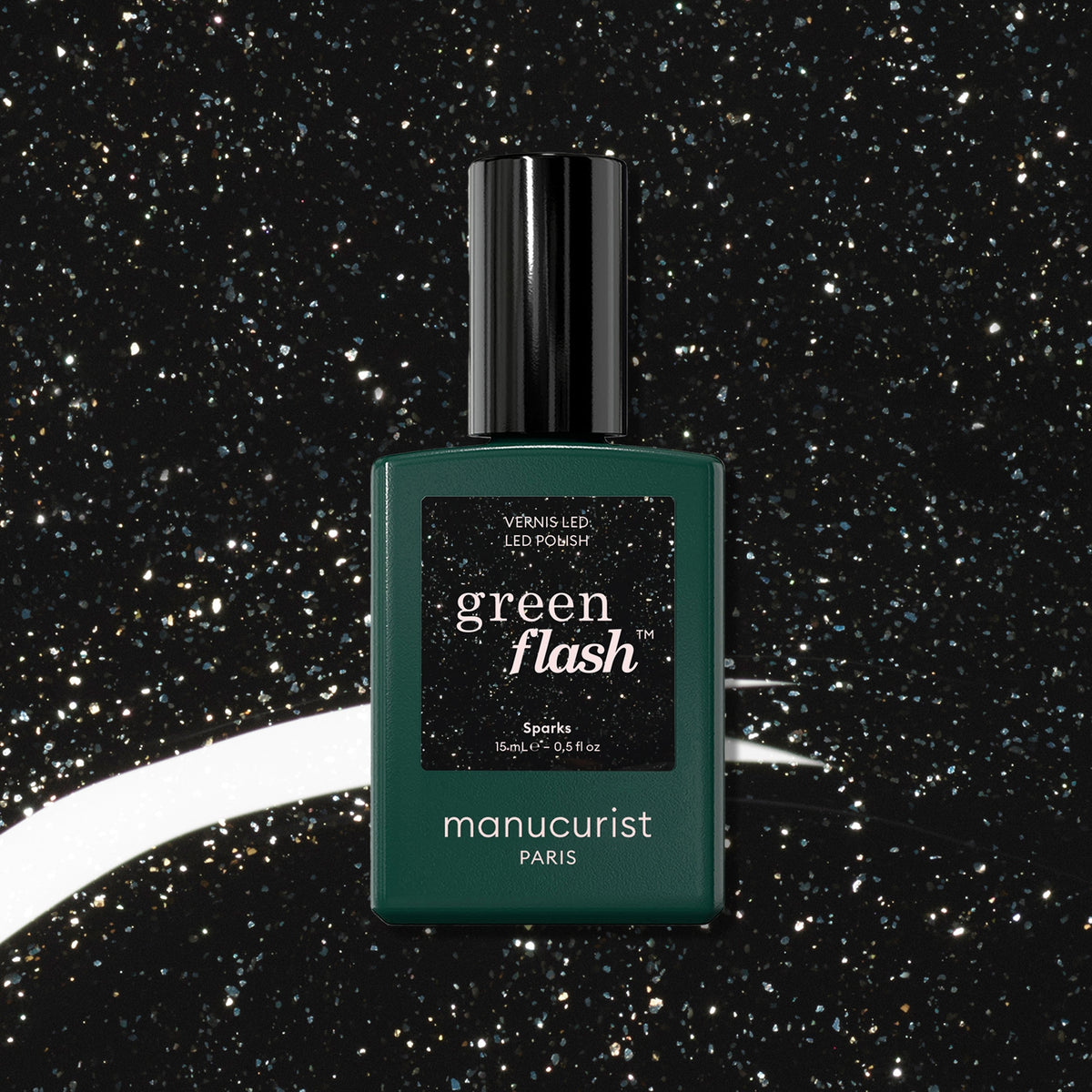 A bottle of Sparks LED gel polish by Manucurist sits against a black, glittery background with white swirls, evoking a starry night sky. The bottle features a dark green hue, black cap, and sharp white text.