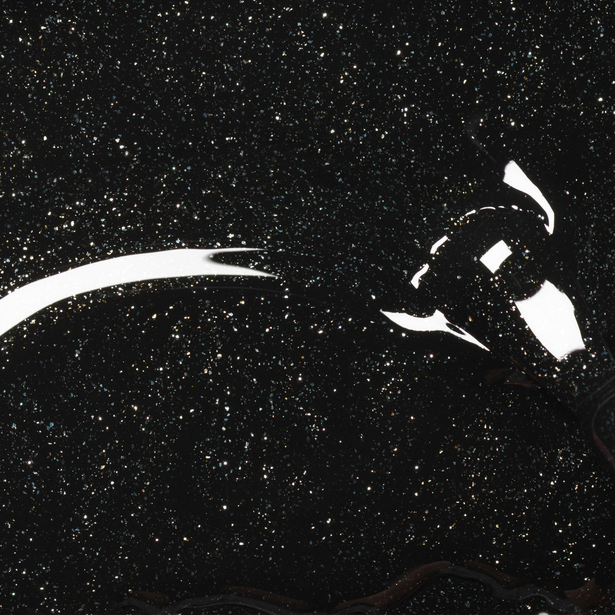 A close-up of Manucurist’s Sparks gel polish—a shimmering black with silver glitter—being applied, creating a glossy, star-like effect on a dark surface.