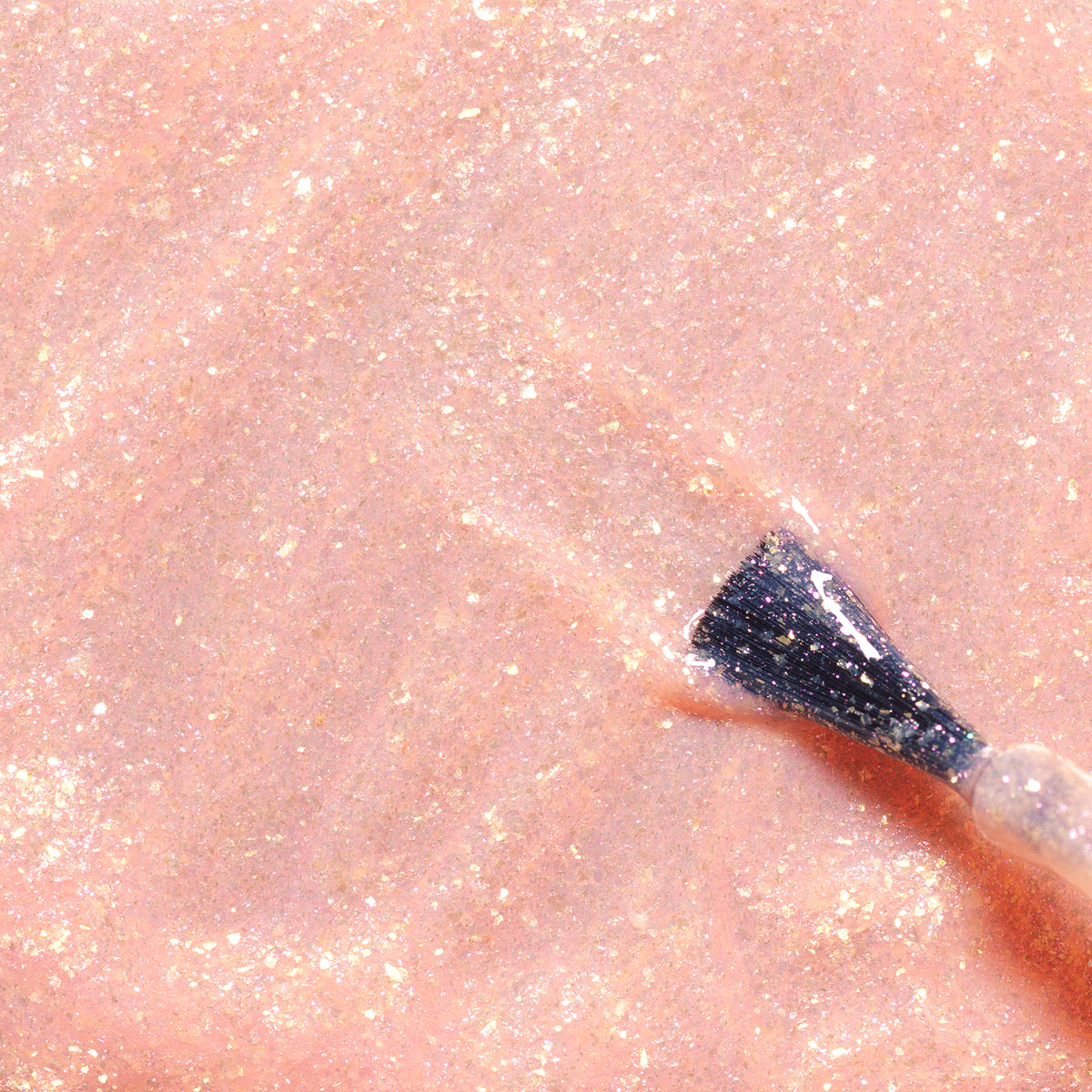 A close-up of Manucurist’s Stella the Starfish brush spreading shimmery, peach nail polish with gold sparkles, glittery pale pink tones, and naturally sourced ingredients.
