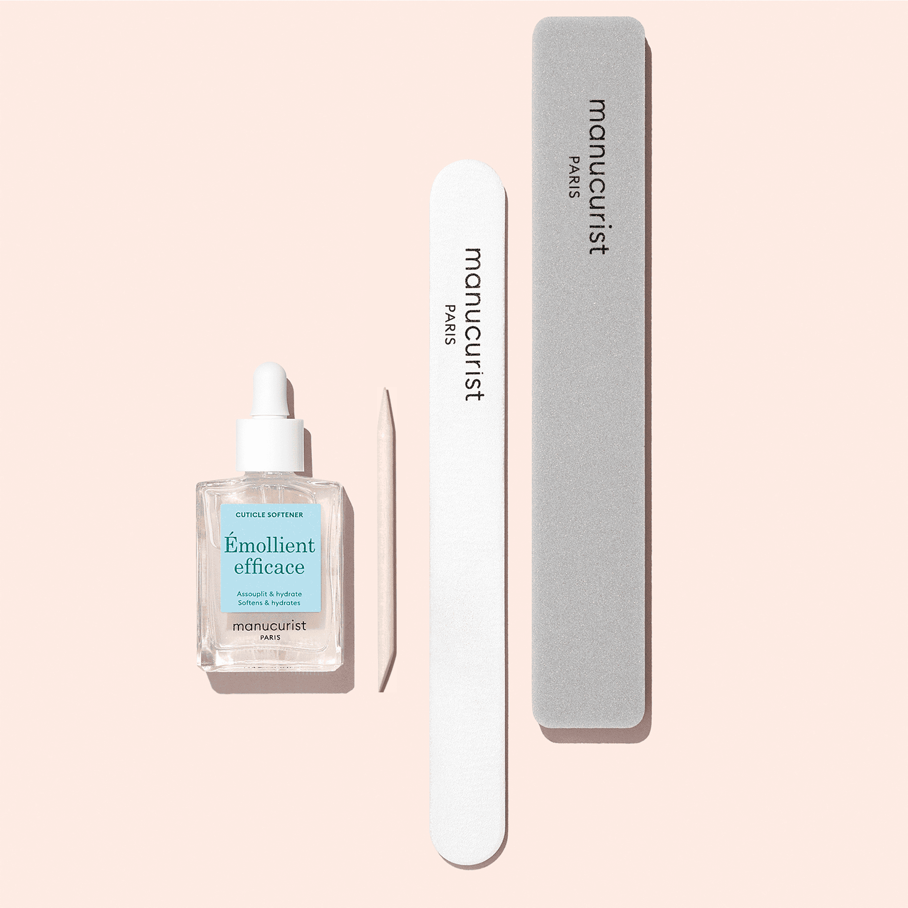 The Manucurist Nail Prep Set—which includes an emollient, a wooden cuticle stick, a white emery board nail file, and a gray nail buffer—is stylishly arranged on a pale pink background.
