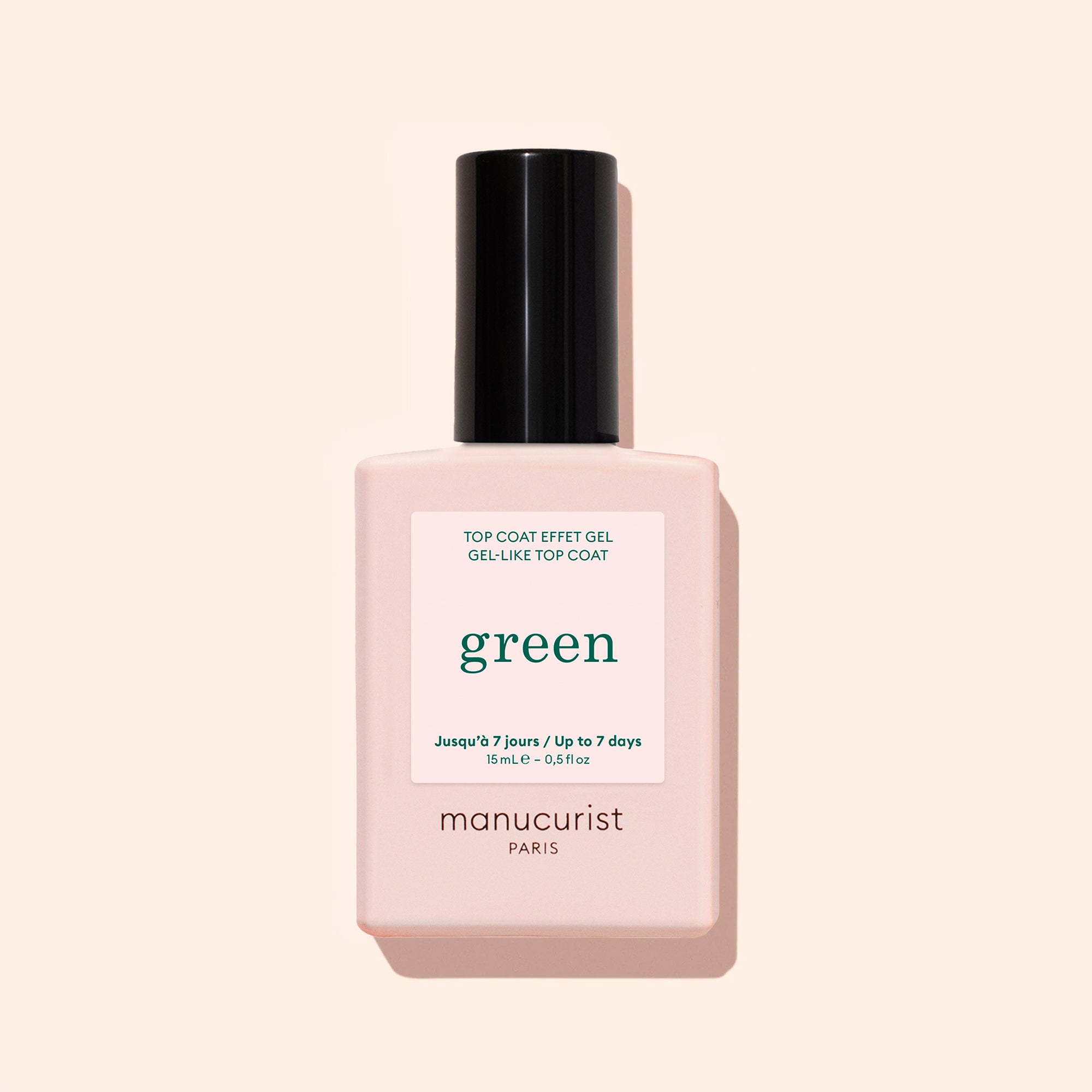 A bottle of Manucurist Sunshine Top Coat, a plant-based, high-shine, long-wear gel-effect nail polish, features a pale pink base and black cap against a beige background.