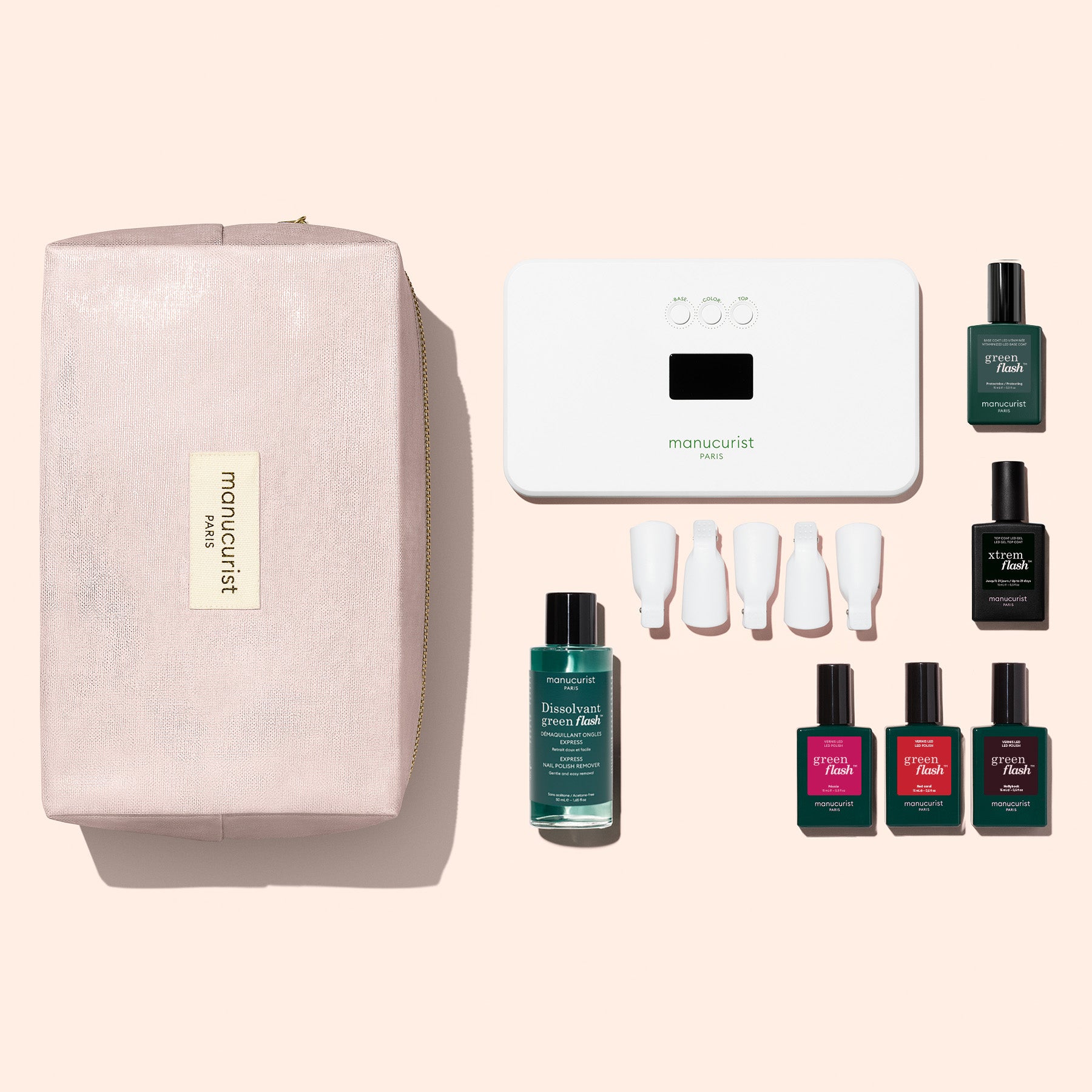 The Manucurist Starter Kit includes a pink zippered pouch, a white LED nail lamp, one bottle of remover, four bottles of gel polish colors, one ultra-glossy top coat, and four white applicator caps—all arranged on a light background.