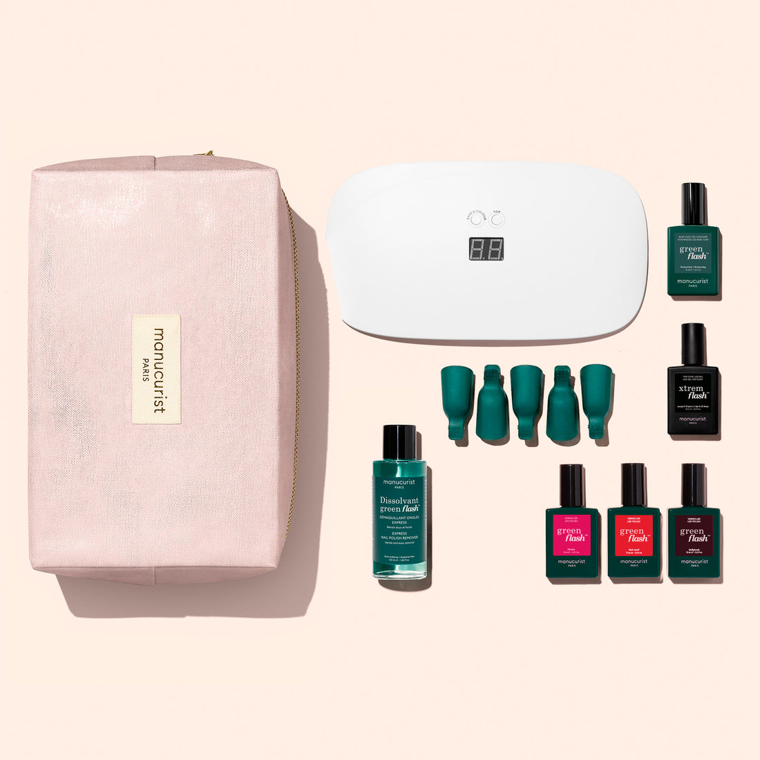 The Manucurist Starter Kit includes a pink pouch, four bottles of nail polish (with one vitamin-infused base coat), a remover bottle, green nail clips, a white LED nail lamp, and a remover solution—all elegantly displayed on a pale pink background for the perfect gel manicure set.