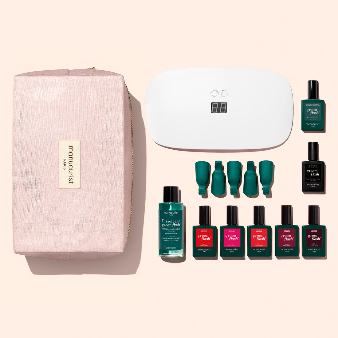 The Manucurist Super Starter Kit features a pink cosmetic bag, a white LED nail lamp, six bottles of Green Flash gel polish in green and red shades offering up to 21 days’ wear, a remover bottle, a vitaminized base coat, and four nail polish caps—all displayed on a light background.