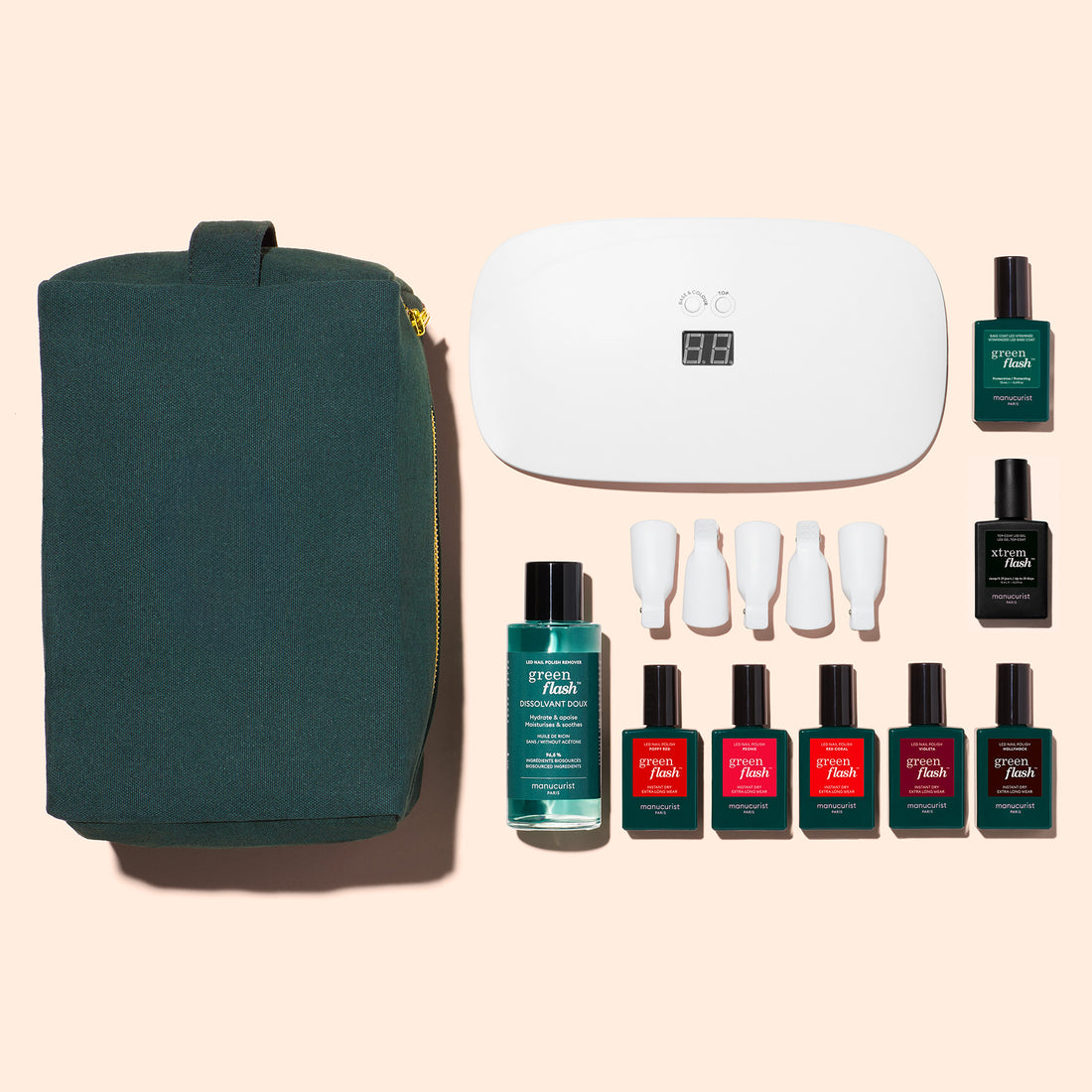 A flat lay of Manucurist’s Super Starter Kit—featuring a green zippered pouch, white LED lamp, nail polish bottles, nail tools, and solution—arranged on a beige background for an ultra-glossy manicure or DIY gel kit.