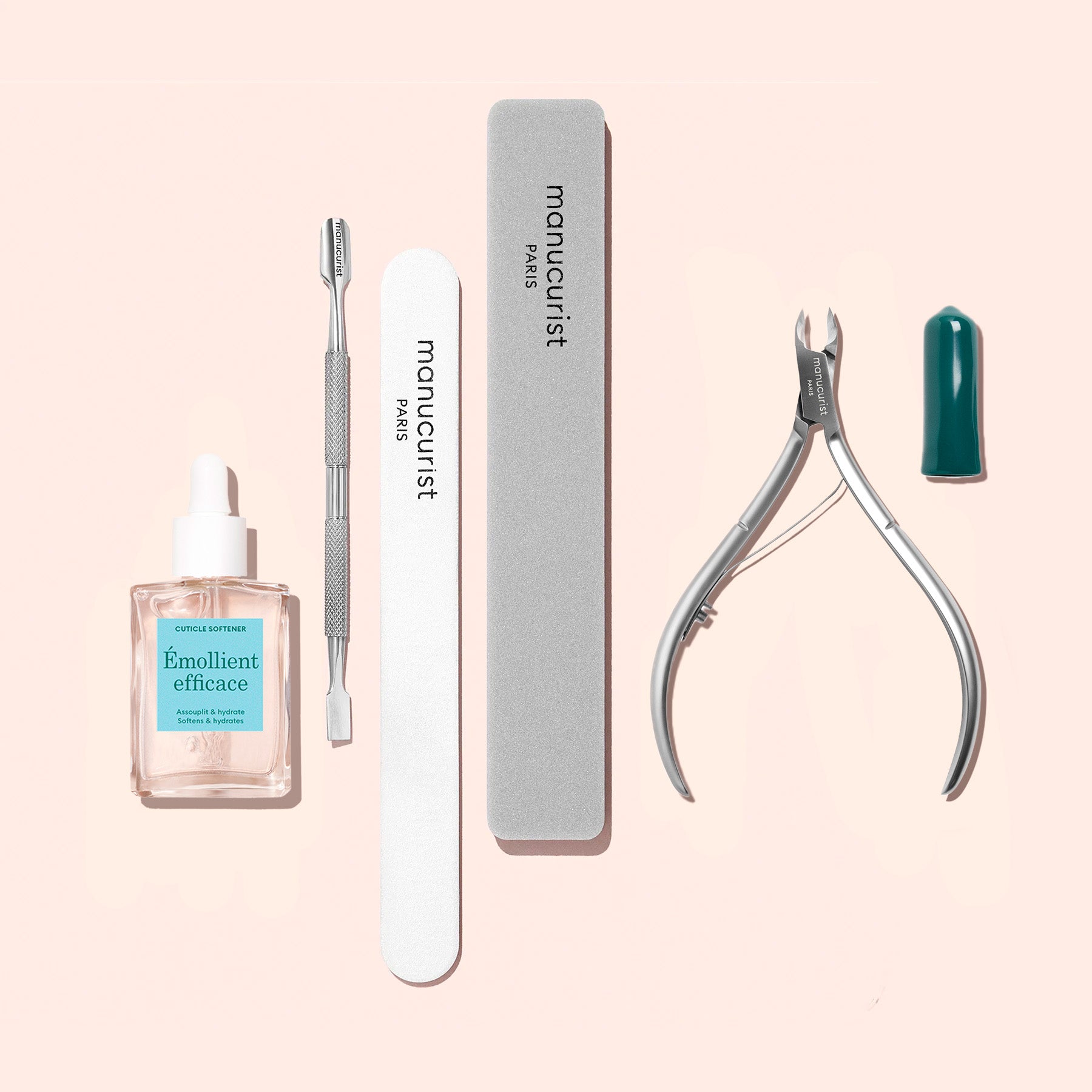The Manucurist Nail Prep Set includes manicure essentials like cuticle oil, an emery board, a metal cuticle pusher, a cuticle nipper, and two nail files—all beautifully presented with a signature green nail polish cap against a light pink background.