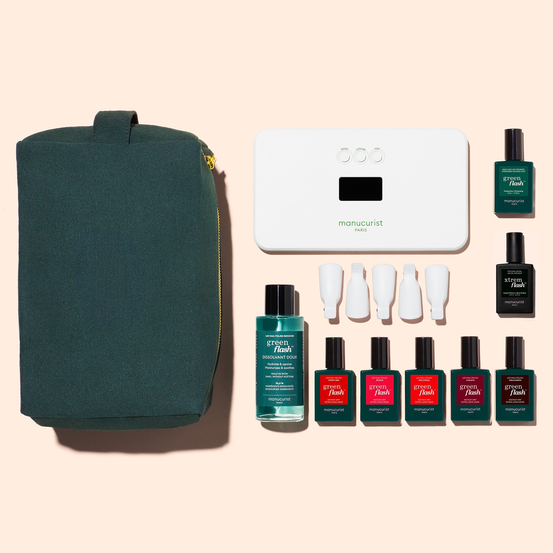 The Manucurist Super Starter Kit features a dark green pouch, a white LED nail lamp, five gel polishes in assorted colors, a Vitaminized Base Coat, and four white caps, all displayed on a light beige background.