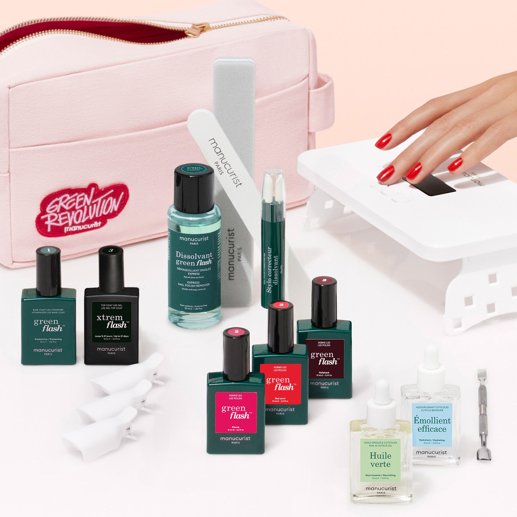 The Manucurist Addict Kit, featuring Green Flash gel polish, nail tools, remover, and oils, is shown beside a pink Green Revolution pouch as a hand with red nails gets an ultra-glossy manicure under a white UV lamp.