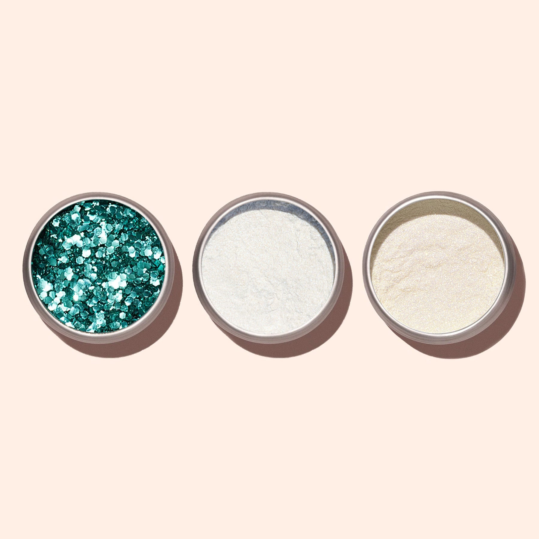 Three round metal containers for nail art powders sit on a light beige background: the left features Manucurist Turquoise biodegradable glitter, the middle contains fine white powder, and the right holds an off-white or beige powder.