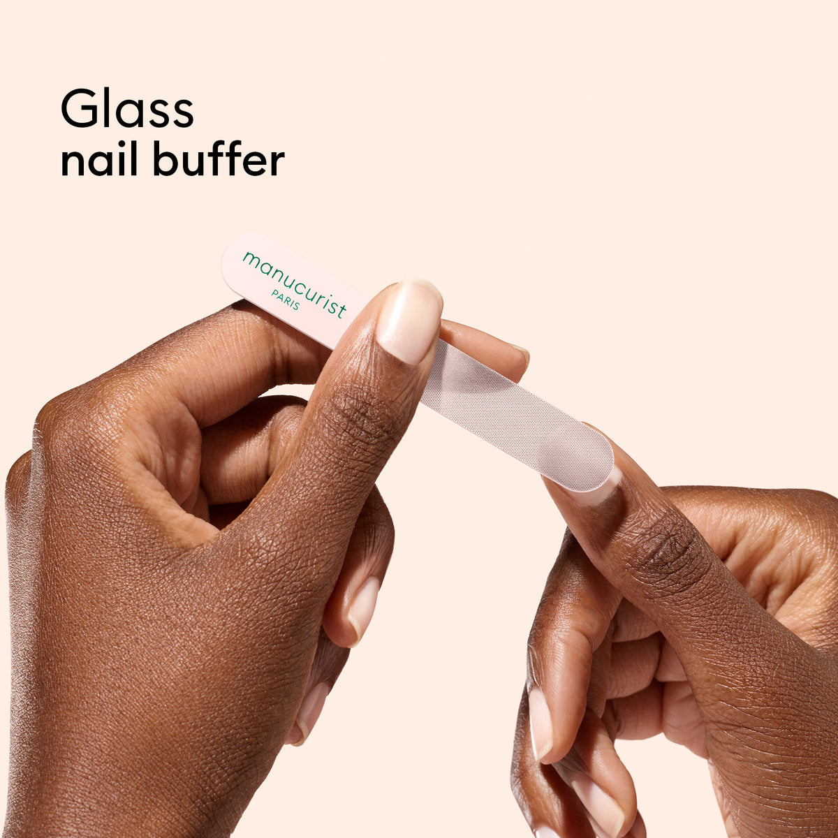 Hands use a Manucurist Glass nail accessory trio to smooth a fingernail, with the text "Glass nail buffer and cuticle pusher" on a beige background.
