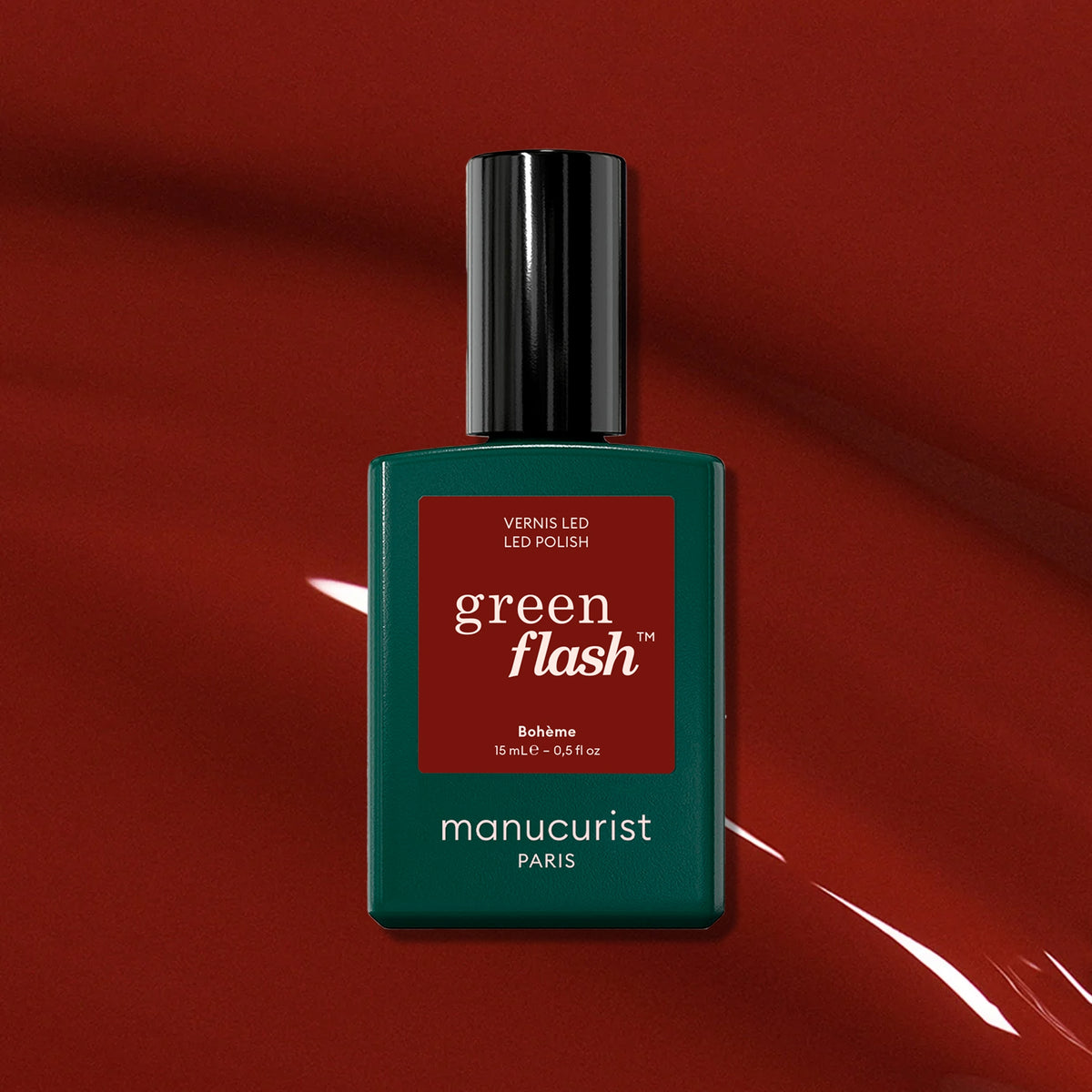 A bottle of Manucurist Bohème, a chic red-brown polish, stands centered on a glossy, deep red background with reflective highlights.