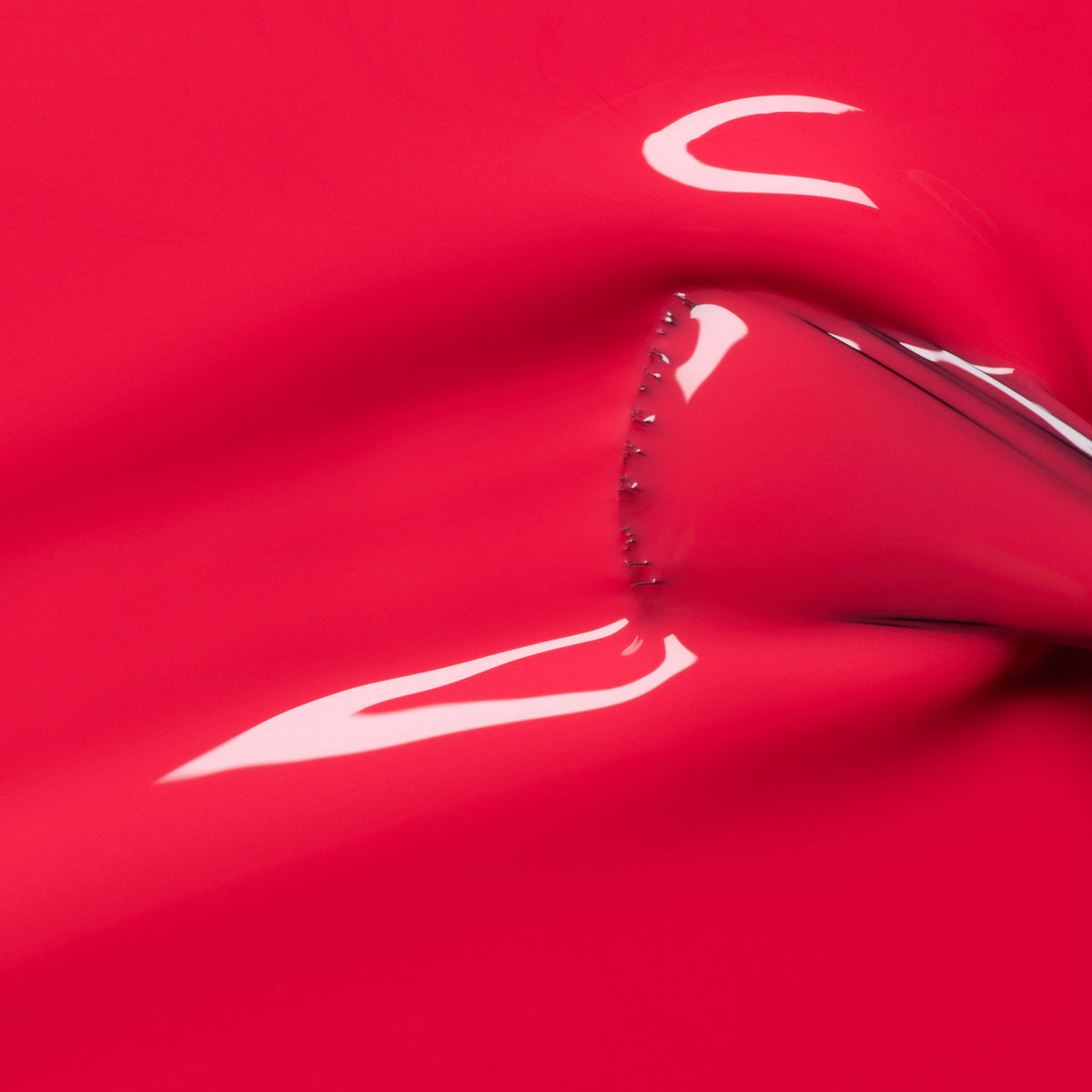 The Bougainvillea by Manucurist features a shiny, smooth bougainvillea-red surface, stretched to reveal reflective curves, tension marks, and small metallic studs accenting the seam.