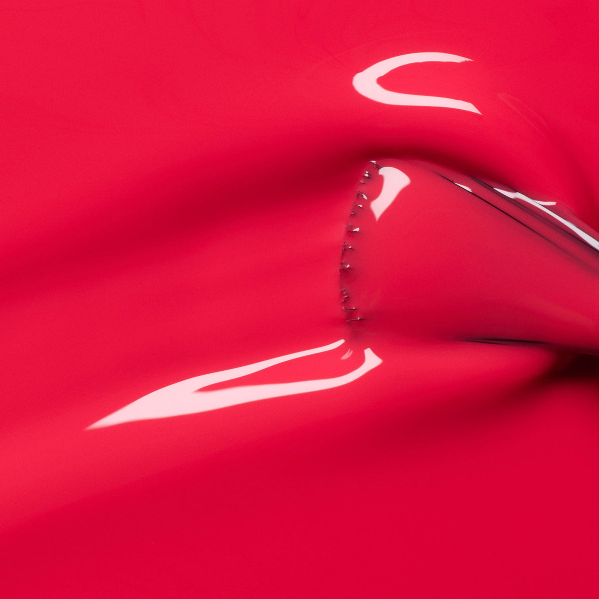 Close-up of Bougainvillea by Manucurist: a shiny, reflective, bright red surface with a seam of small studs—evoking bougainvillea petals or glossy reddish-pink nail polish in an abstract, smooth finish.